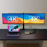 mbeat MB-DLA-CD2H adapter connecting a MacBook Pro to two monitors mounted on a dual monitor arm, both screens displaying 4K badge graphics, demonstrating true dual 4K extended display output.